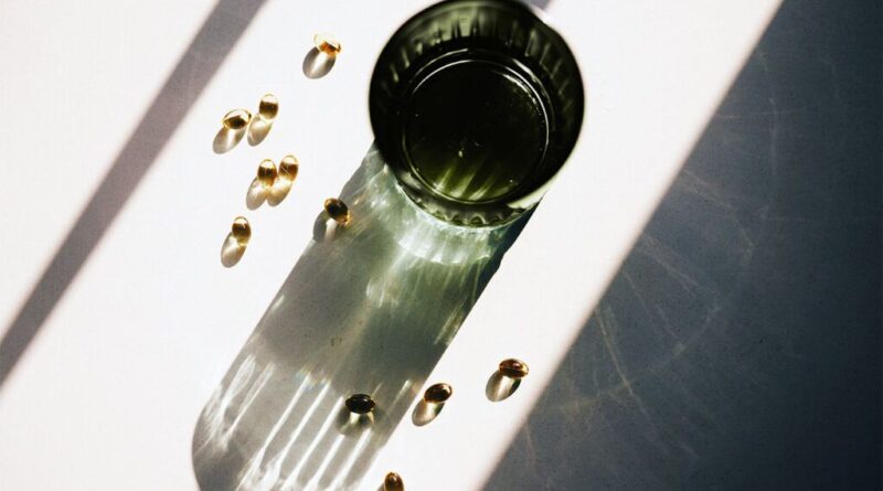 Vitamin D capsules are spilled next to a green glass cup