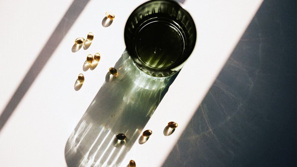 Vitamin D capsules are spilled next to a green glass cup